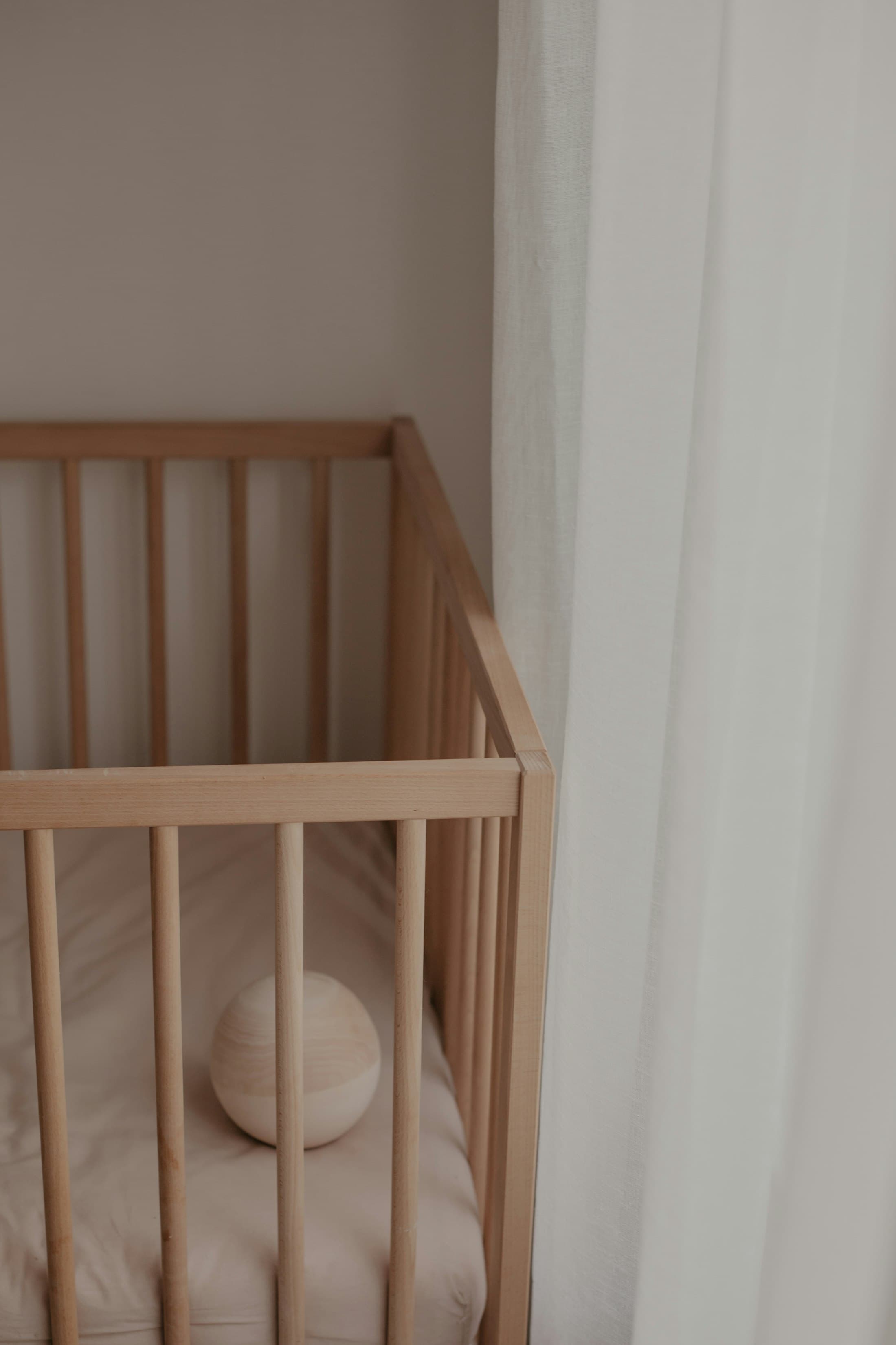 A natural wood crib beside a linen curtain in soft window light